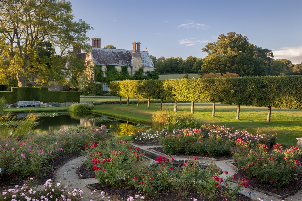 sunset view of batemans formal gardens with old visible above hedgerows